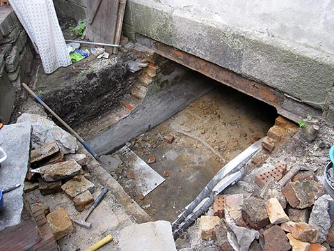 Очищенная выгребная яма. Кирпичи по периметру ямы наполовину разобраны. Под гранитным блоком ржавое перекрытие.